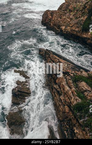 Une vue aérienne spectaculaire d'une côte rocheuse où de puissantes vagues océaniques s'écrasent contre des falaises escarpées. Le paysage marin dynamique capture la beauté brute et R Banque D'Images