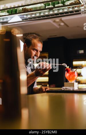 Un barman habile crée un cocktail, en se concentrant intensément sur la tâche. Ils travaillent dans un cadre de bar moderne, entouré de bouteilles et de verrerie, showcas Banque D'Images
