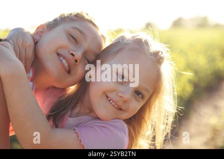 Portrait en gros plan de deux sœurs serrées chaleureusement, rayonnant de bonheur dans un champ de fleurs ensoleillé dont les expressions capturent la pureté de l'enfance Banque D'Images