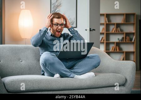 Célébrer le succès. Travailleur indépendant masculin utilise un ordinateur portable à la maison. Appartement confortable. Banque D'Images
