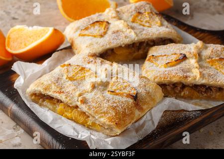 Tarte à la pâte feuilletée à l'orange maison avec noix, raisins secs et fruits frais gros plan sur planche de bois sur la table. Horizontal Banque D'Images