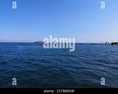 Une vue sereine sur l'océan avec un ciel bleu clair et des îles lointaines. Plusieurs petits bateaux sont ancrés près du rivage, créant une scène maritime paisible. Banque D'Images