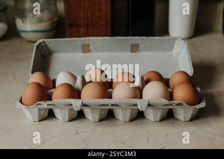 Carton plein d'oeufs bruns et blancs frais de ferme assis sur le comptoir de la cuisine Banque D'Images