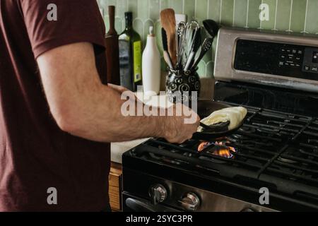 plan large d'un homme cuisant des œufs pour le petit déjeuner sur sa cuisinière à gaz Banque D'Images