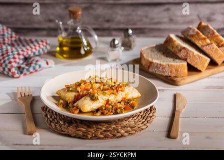 Filets de merlu avec légumes sautés, accompagnés de pain et sur une table blanche rustique. Banque D'Images