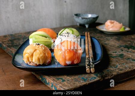 Temari sushi. Boules de sushi tendance avec saumon, avocat, concombre et omelette japonaise sur assiette bleue. Sauce soja, gingembre mariné, baguettes sur WO rustique Banque D'Images