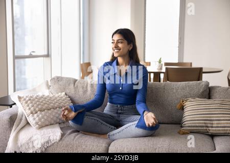 Jeune femme assise les jambes croisées sur le canapé en posture méditative Banque D'Images