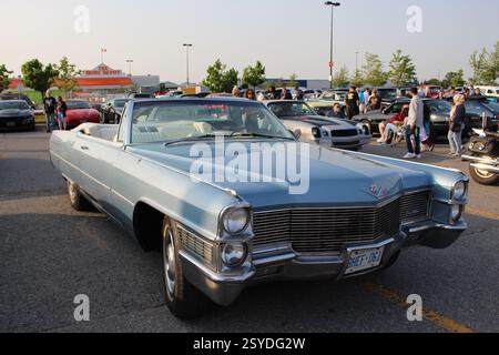 Un cabriolet Cadillac bleu clair classique garé lors d'un salon automobile animé. Passionnés et spectateurs admirent les véhicules vintage et modernes sous un ciel dégagé. Banque D'Images