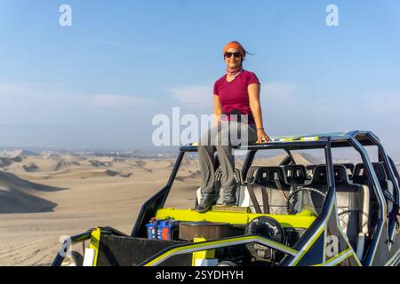 Une femme assise sur un buggy à Huacachina Oasis à ICA Pérou entourée de dunes de sable et de palmiers Banque D'Images