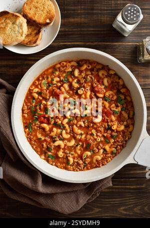 Goulash américain, plat avec boeuf haché, légumes et pâtes en sauce tomate dans une poêle sur table en bois. Vue de dessus, pose à plat Banque D'Images