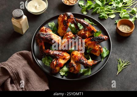 Ailes de poulet BBQ sur plaque noire sur fond de pierre sombre. Savoureuse viande de poulet grillée pour le dîner. Vue rapprochée Banque D'Images