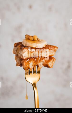 Une bouchée dorée de la perfection du brunch : gaufres croustillantes garnies de banane, de noix et d'un filet de sirop de rêve Banque D'Images