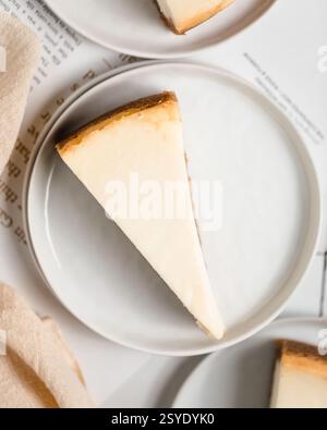 Tranche de cheesecake classique à la croûte dorée servie sur une simple assiette blanche sur une table minimaliste. Banque D'Images