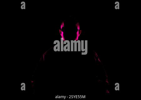 Une silhouette éclairée de manière créative d'une personne, représentée en utilisant des teintes roses vibrantes contre l'obscurité, évoquant mystère et drame. Banque D'Images