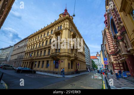 Une prise de vue sous un angle bas capture un bâtiment historique d'angle avec une façade ornée et un toit rouge, sous un ciel lumineux, à côté d'un bâtiment moderne rayé et d'un stre Banque D'Images
