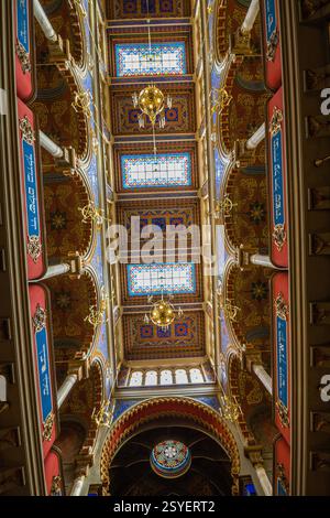 Une photo verticale d'un plafond intérieur orné avec une série de sections cintrées avec des motifs décoratifs, des vitraux et des lampes suspendues Banque D'Images