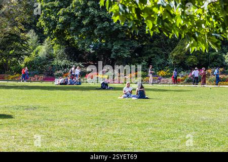 Scène de parc dynamique avec des gens se relaxant sur l'herbe verte entouré par la nature et les fleurs Banque D'Images