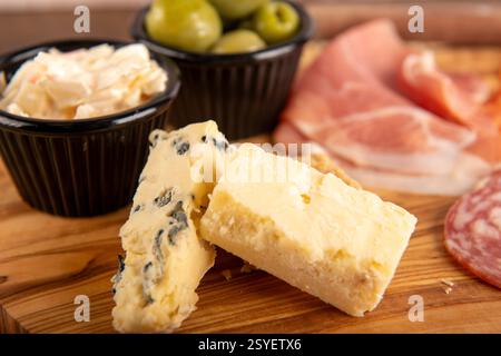 Une assiette de fromages avec une variété de fromages et d'olives. Le fromage est coupé en petits morceaux et disposé sur une planche à découper en bois Banque D'Images