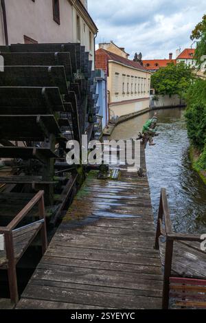 Un moulin à eau historique avec une grande roue en bois se trouve à côté d'un canal dans une vieille ville européenne, mettant en valeur l'ingénierie et l'architecture traditionnelles. Banque D'Images