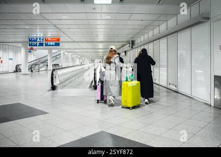 Munich, Bavière, Allemagne - 26 février 2025 : les voyageurs avec des valises colorées traversent une allée presque vide de l'aéroport pour se rendre à la zone de départ *** Reisende mit bunten Koffern gehen durch einen fast leeren Gang im Flughafen, während sie sich zum Abflugbereich bewegen Banque D'Images