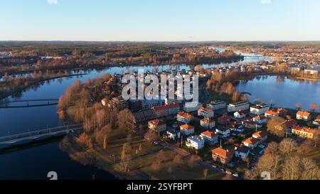 Une vue aérienne époustouflante de Karlstad, en Suède, mettant en valeur les rivières, les ponts et les charmantes maisons aux toits rouges, baignées de lumière dorée chaude du coucher de soleil, créant un paysage nordique paisible et pittoresque. Banque D'Images