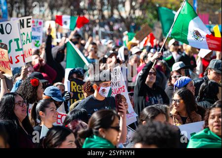 Un jeune homme avec un masque facial avec drapeau mexicain écoute dans la foule à la manifestation pro-immigrant dans le centre-ville au parc Cesar Chavez. Banque D'Images