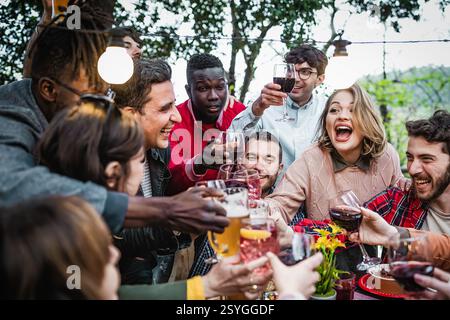 Un groupe joyeux d'amis divers levant des verres et grillant lors d'un dîner en plein air, partageant rire et bonheur. Ambiance festive avec dri Banque D'Images