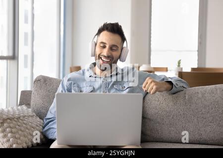 Homme porte des écouteurs regardant un film ou du contenu en streaming à l'aide d'un ordinateur portable Banque D'Images