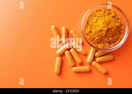 Poudre de curcuma dans un bol et capsules sur fond orange, plat. Espace pour le texte Banque D'Images