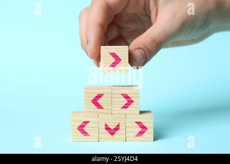 Femme empilant des cubes en bois avec des flèches roses sur fond bleu clair, gros plan Banque D'Images