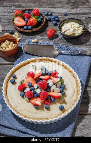Tarte aux baies avec croûte à base de massepain et remplissage de crème d'amande de noix de coco dans une assiette à tarte en céramique sur une table en bois rustique avec pelle à gâteau et baies fraîches, Banque D'Images