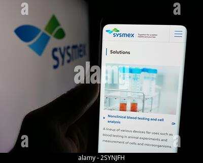 Dans cette illustration photo, une personne tient un téléphone portable avec la page Web de la société japonaise de soins de santé Sysmex Corporation sur l'écran avec logo. Banque D'Images