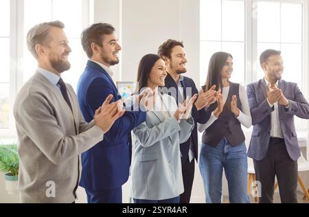 Groupe de gens d'affaires applaudissant des mains et souriant tout en assistant à un séminaire d'entreprise ou à une formation. Banque D'Images