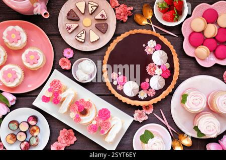 Scène de table de fête des mères avec une collection de desserts et de bonbons. Vue de dessus sur un fond de bois sombre. Thème fleurs roses. Banque D'Images