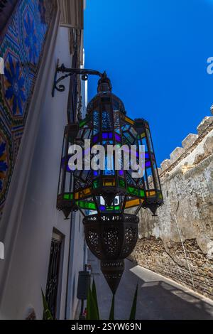 Lanterne marocaine vibrante avec panneaux de vitraux colorés, projetant des ombres complexes contre un mur blanchi à la chaux et ajoutant une touche de couleur vibrante Banque D'Images