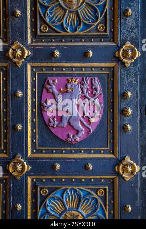 Gros plan d'une porte ornée représentant un emblème héraldique de lion dans un écusson, entouré d'éléments métalliques décoratifs sur une texture sombre Banque D'Images
