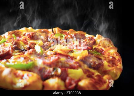 Pizza avec du bacon au jambon au fromage et pepperoni sur fond noir isolé avec de la fumée chaude à la vapeur. Concept de nourriture et de cuisine. Déjeuner Banque D'Images