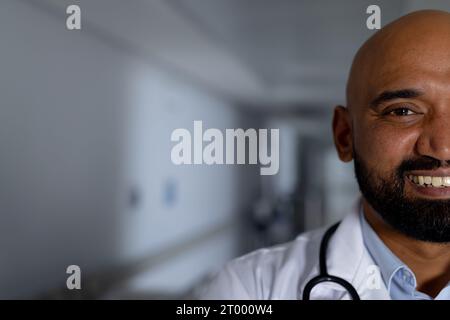 Portrait d'un médecin homme biracial heureux portant une blouse de laboratoire dans le couloir à l'hôpital, espace de copie Banque D'Images