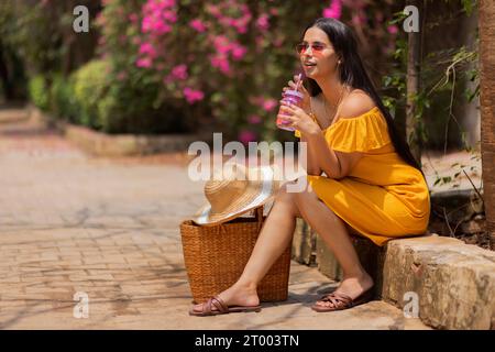 Femme buvant de l'eau détox en étant assise dans le parc Banque D'Images