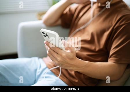 Détendu jeune homme asiatique amateur de musique assis en écoutant de la musique sur des écouteurs. Homme tenant le téléphone portable dans le salon écoutant m Banque D'Images