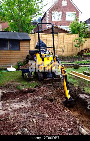 Mini pelle garée dans un jardin utilisé pour creuser le sol pour construire un conservatoire, Chard, Somerset, Royaume-Uni, Europe. Banque D'Images