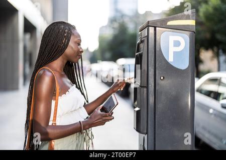 Jeune femme utilisant le parcmètre sur une rue de la ville Banque D'Images