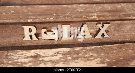 lettres en bois nature au soleil sur une journée heureuse ensoleillée. créez un texte de mot à partir d'alphabet de lettre en bois. Fond naturellement en bois, les lettres SE DÉTENDENT Banque D'Images