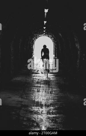 Cycliste sur le vélo de route dans le tunnel étroit. Silhouette d'athlète. Photographie en noir et blanc. Banque D'Images