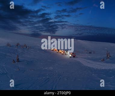 Tondeuses à neige (machines à ratraquer) en excursion nocturne avant l'aube jusqu'au sommet de la montagne en hiver avec des snowboarders freeriders. Al Banque D'Images