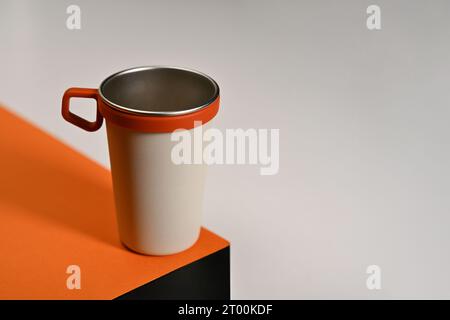 Tasse de voyage en céramique blanche avec support en silicone sur table orange. Récipient à boisson Tumbler et concept écologique Banque D'Images