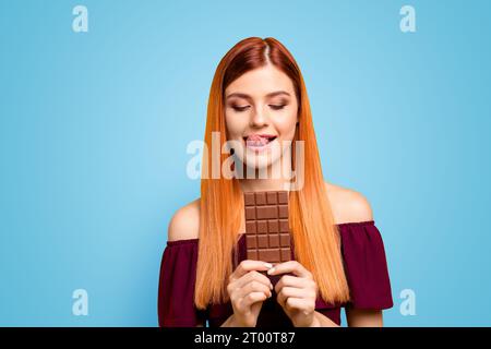 Jeune fille aux cheveux rouges tenant une barre de chocolat isolée sur fond jaune Banque D'Images