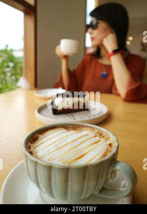Gros plan d'une tasse de Macchiato au caramel chaud avec une femme buvant du café en toile de fond Banque D'Images