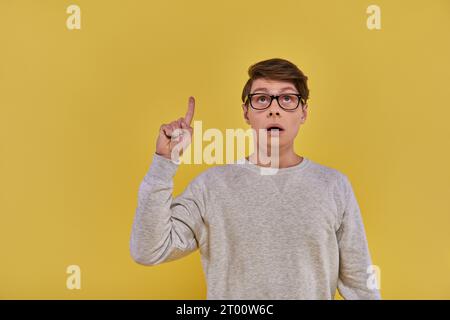 jeune homme en sweat-shirt blanc levant le doigt dans le geste eureka et regardant vers le haut sur fond jaune Banque D'Images