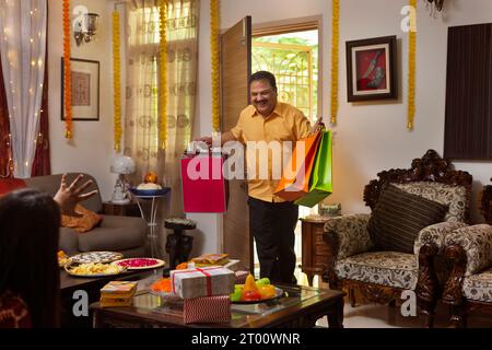 L'homme entre heureux dans la maison avec des cadeaux et des sacs à provisions pour sa famille, pendant le festival de Diwali Banque D'Images